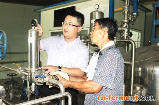 刘泽凯(右)在检修中的微生物农药生产设备前,与工作人员讨论设置参数。